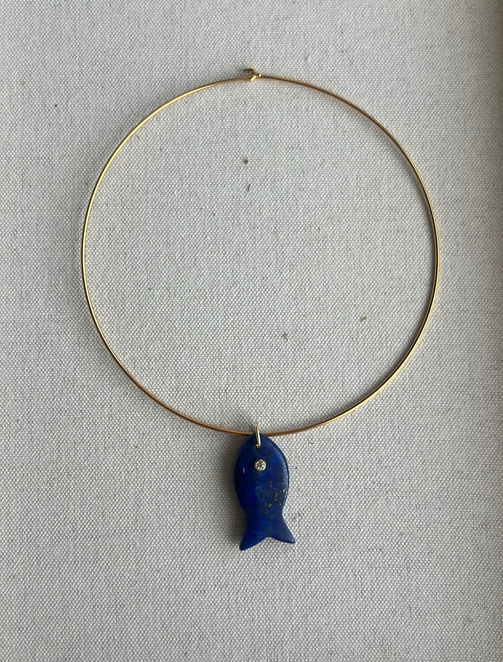 Gold necklace with a blue fish pendant on a gray background