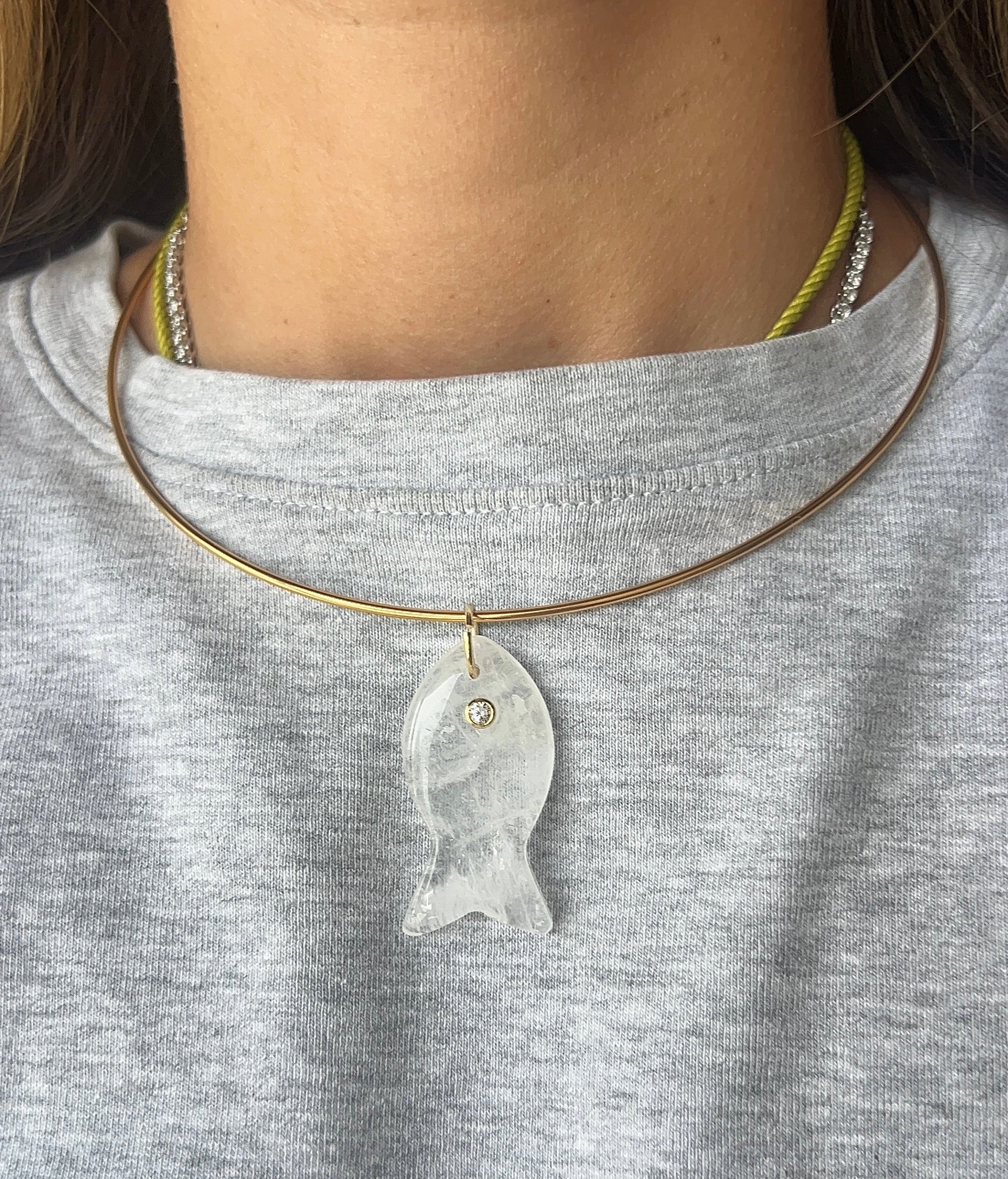 Necklace with a fish pendant worn by a person on a gray shirt